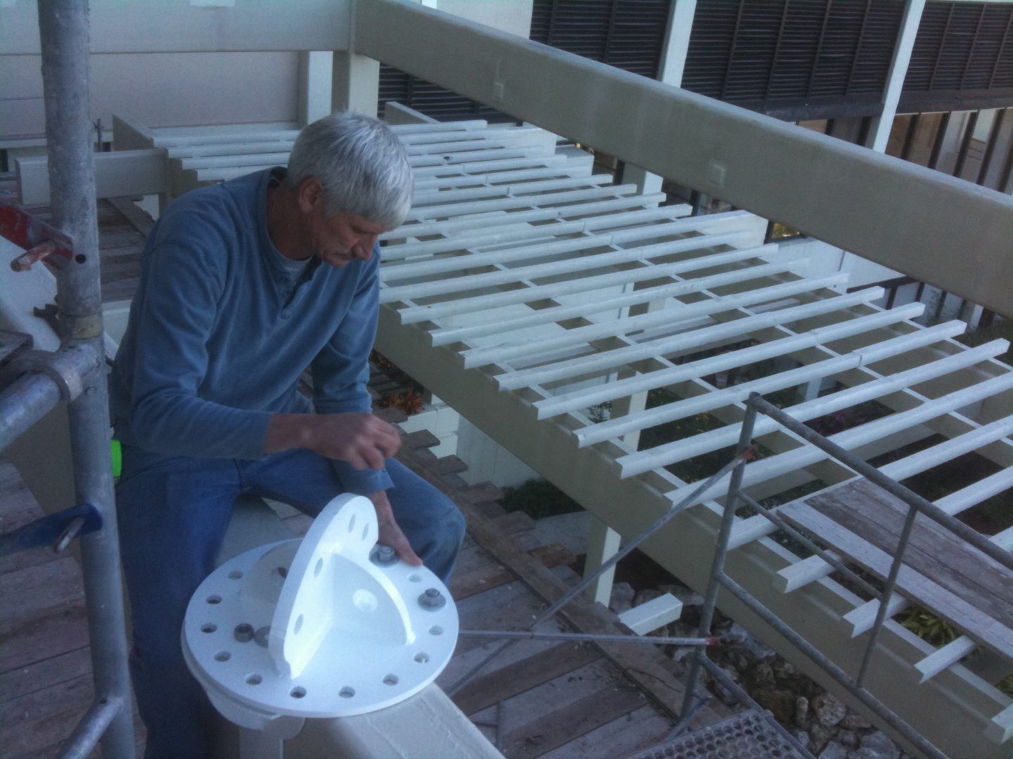 An elderly man assembling a white mechanical structure indoors.