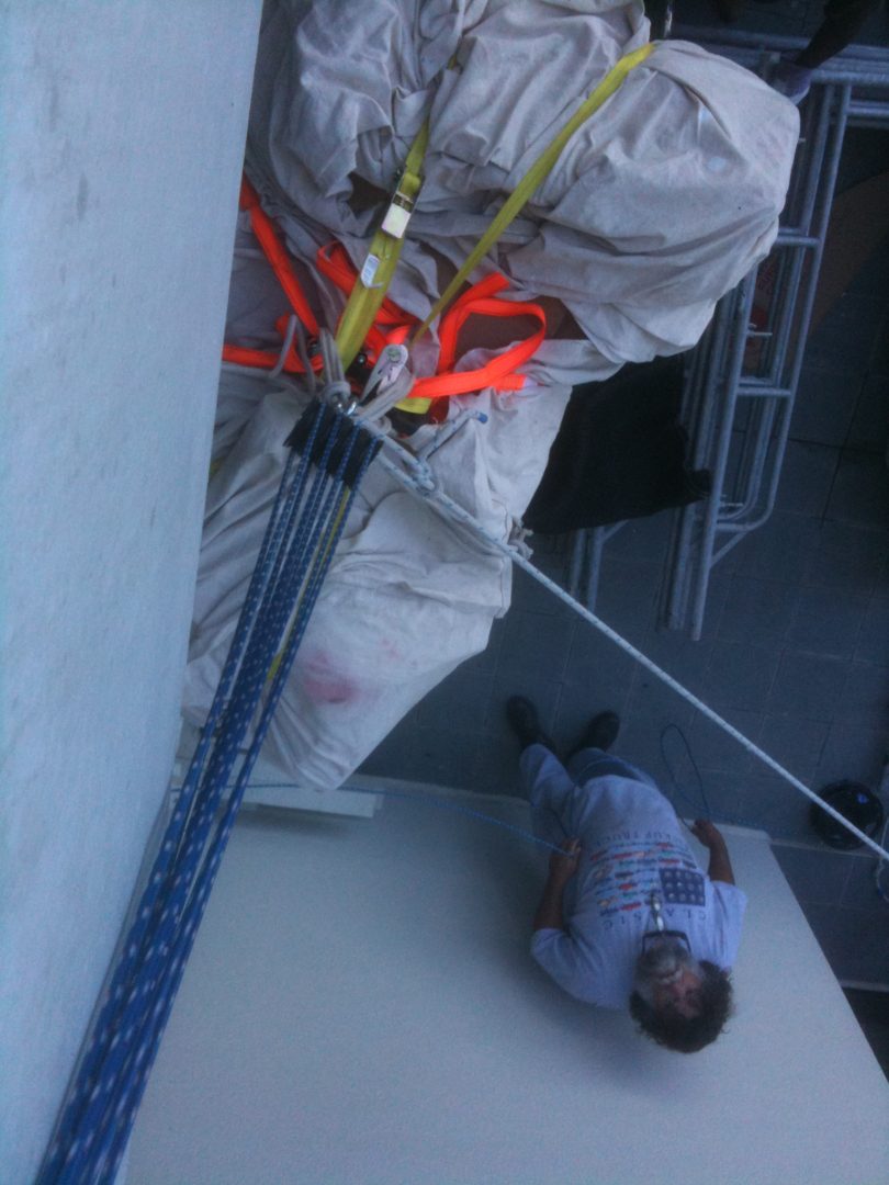 Worker climbing a rope wearing safety gear and a helmet.