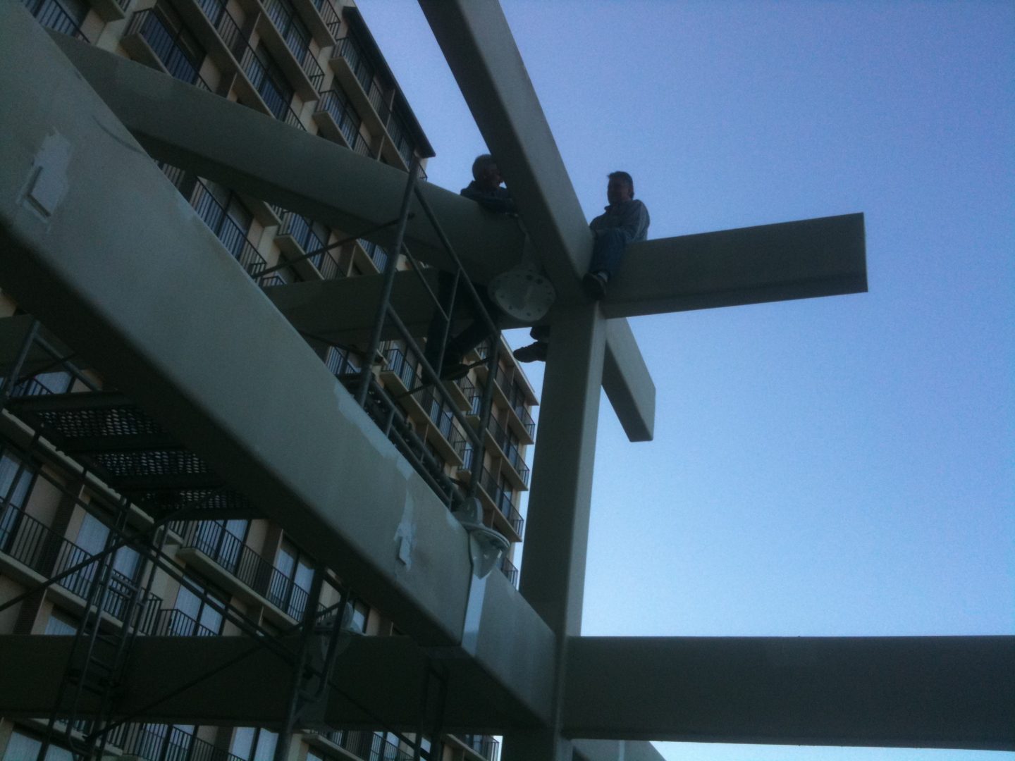 Construction workers installing steel beams on a building frame under clear sky.