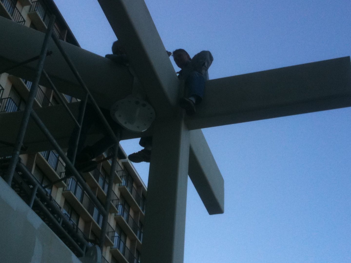 Person sitting on a large cross structure against the evening sky.