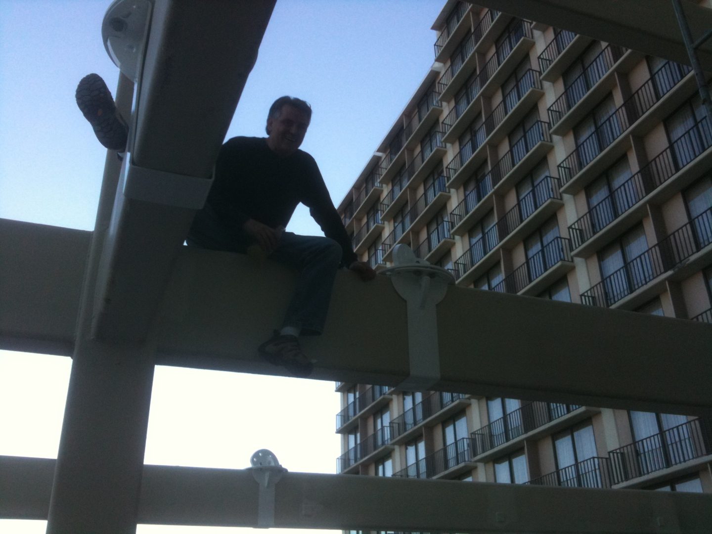 Person sitting on a beam in an urban setting with a tall building in the background.