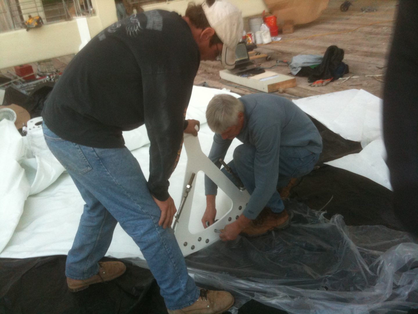 Two men working together on a large piece of fabric indoors.
