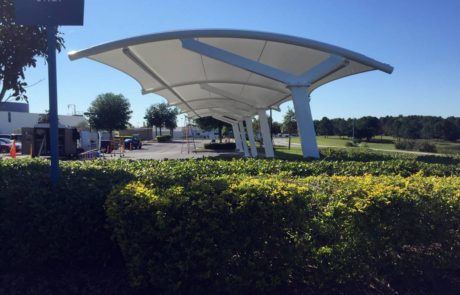 Modern shaded walkway structure near a green hedge under a clear sky.