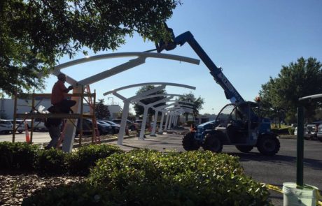 Workers assembling a large metal structure outdoors with a crane.
