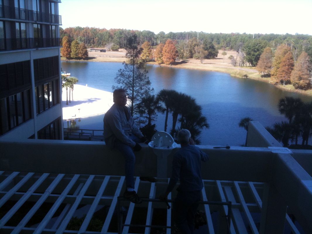 Two people on a balcony overlooking a lake and trees.