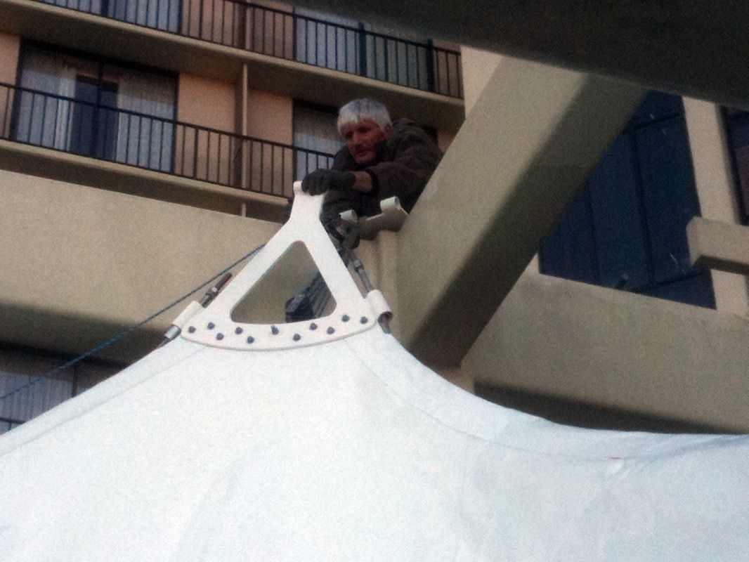 Person working on a large white tent outdoors.