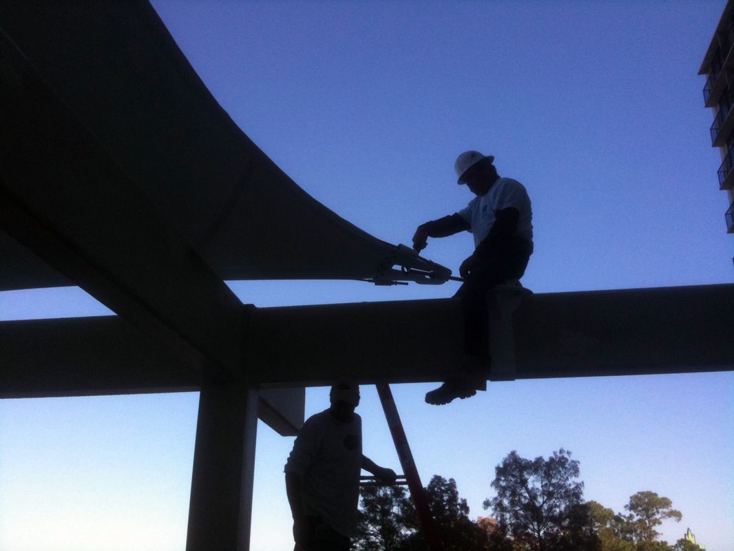 Two people working on a construction beam during dusk.
