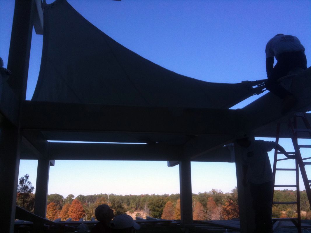 Silhouette of a person adjusting a tarp on a wooden structure at sunset.