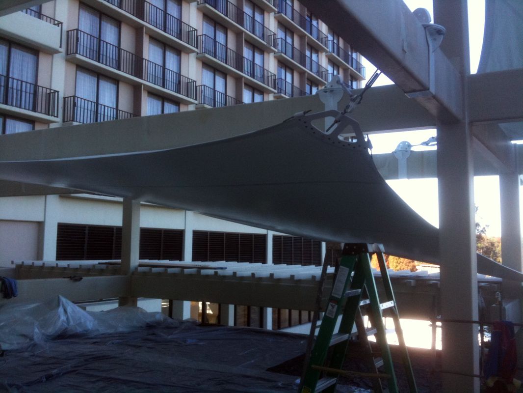 Ladder under a large outdoor shade sail near a building.