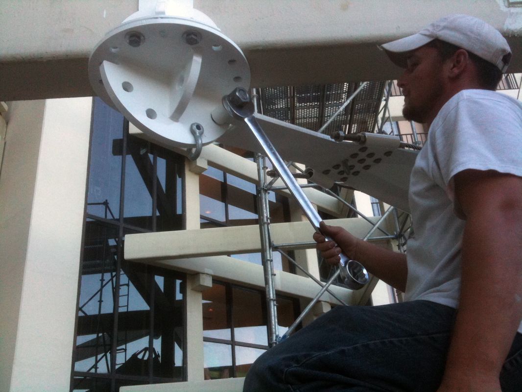 Man adjusting large satellite dish outdoors near a building under construction.