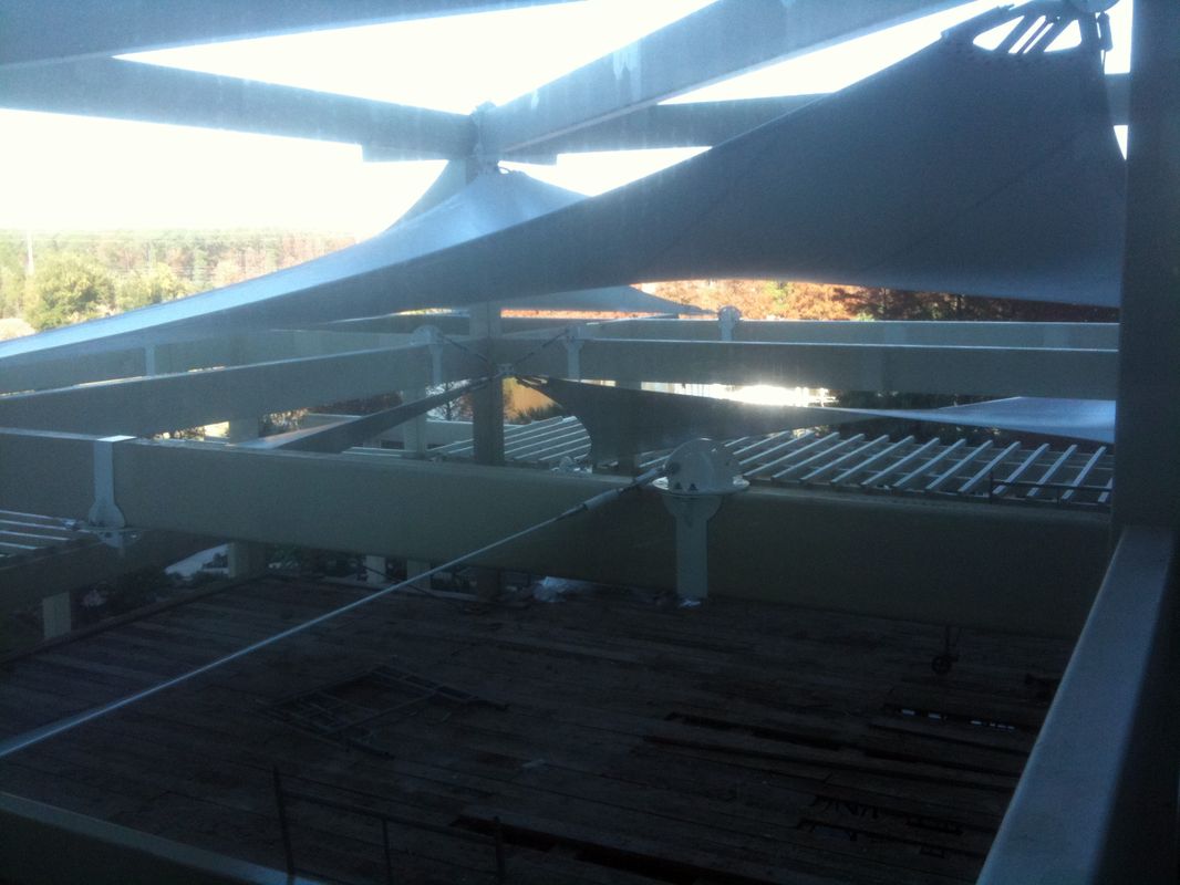 View under a sail-like structure with beams and a distant water body.